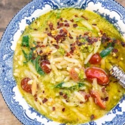 pesto lemon orzo soup in a blue and white bowl, topped with red pepper flakes