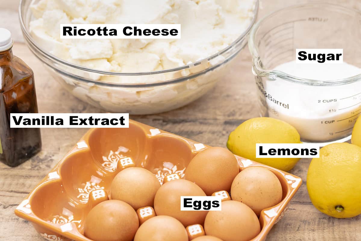 labeled ingredients for ricotta cheesecake including whole-milk ricotta, sugar, lemons, eggs, and vanilla extract