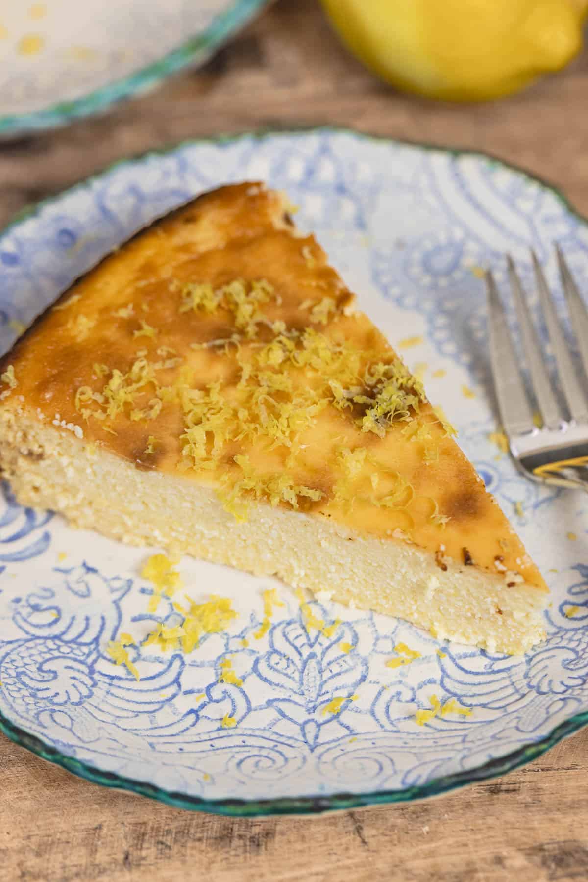 slice of Italian cheesecake on a small plate with a sprinkle of lemon zest. Fork on the side