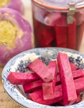 pink pickles in a small plate with a jar of pickled turnips and whole fresh turnips in the background