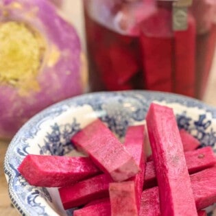 pink pickles in a small plate with a jar of pickled turnips and whole fresh turnips in the background