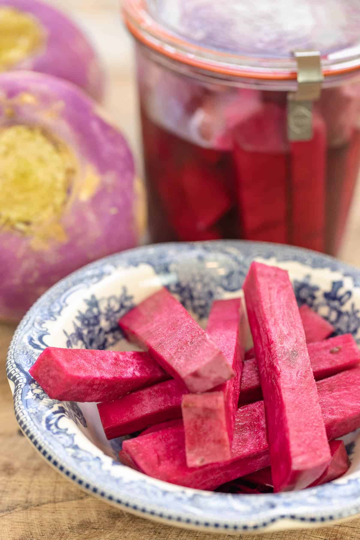 pink pickles in a small plate with a jar of pickled turnips and whole fresh turnips in the background