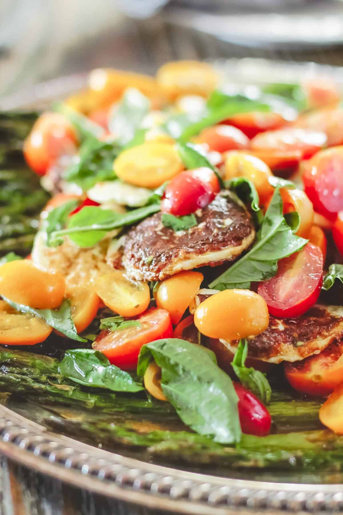 roasted asparagus salad with cherry tomatoes, halloumi cheese, and basil leaves on a platter