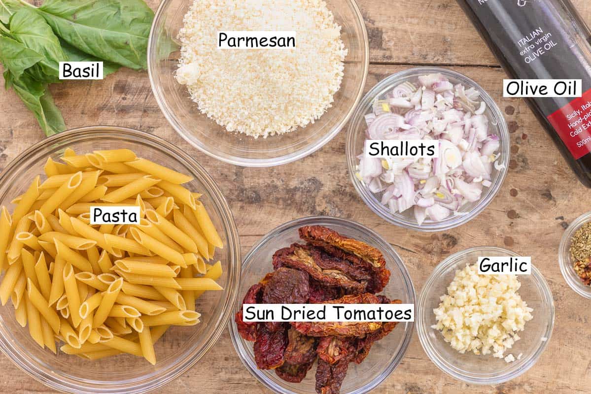 labeled ingredients for sundried tomato pasta including olive oil, shallots, herbs, garlic, sun-dried tomatoes, pasta, parmesan cheese, and fresh basil