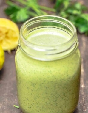 green tahini sauce in a Mason jar with parsley and lemon in the background