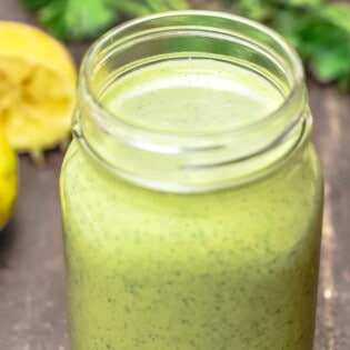 green tahini sauce in a Mason jar with parsley and lemon in the background