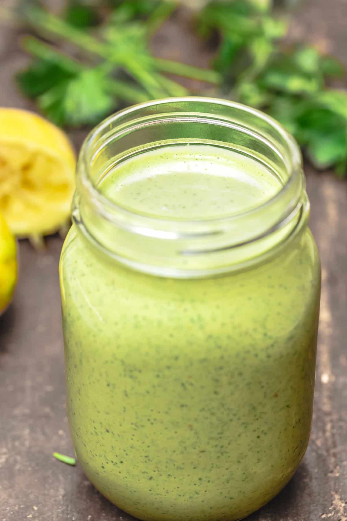 green tahini sauce in a Mason jar with parsley and lemon in the background