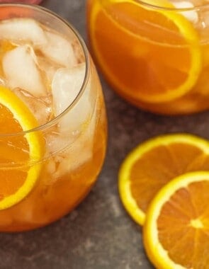 two aperol cocktails with fresh orange slices next to them.