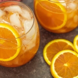 two aperol cocktails with fresh orange slices next to them.