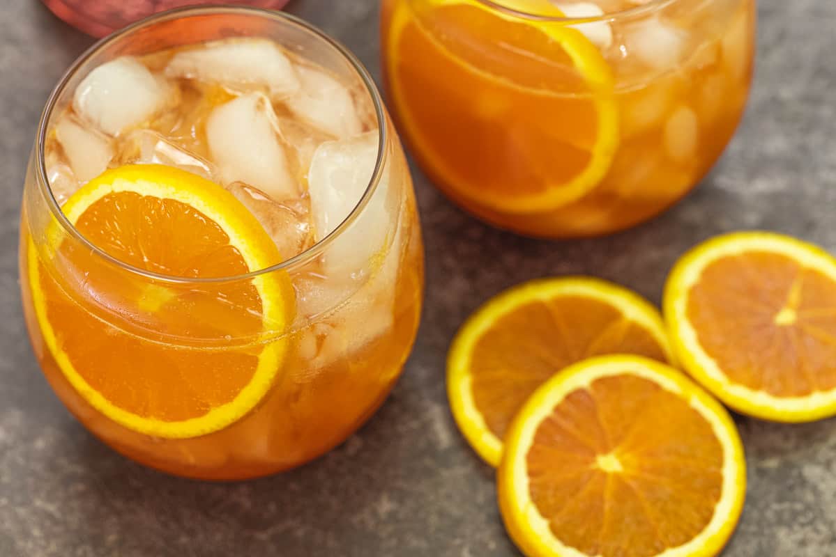 two aperol cocktails with fresh orange slices next to them.