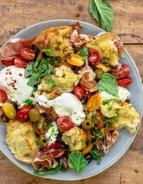 burrata salad on a gray plate with some fresh basil leaves on the side.