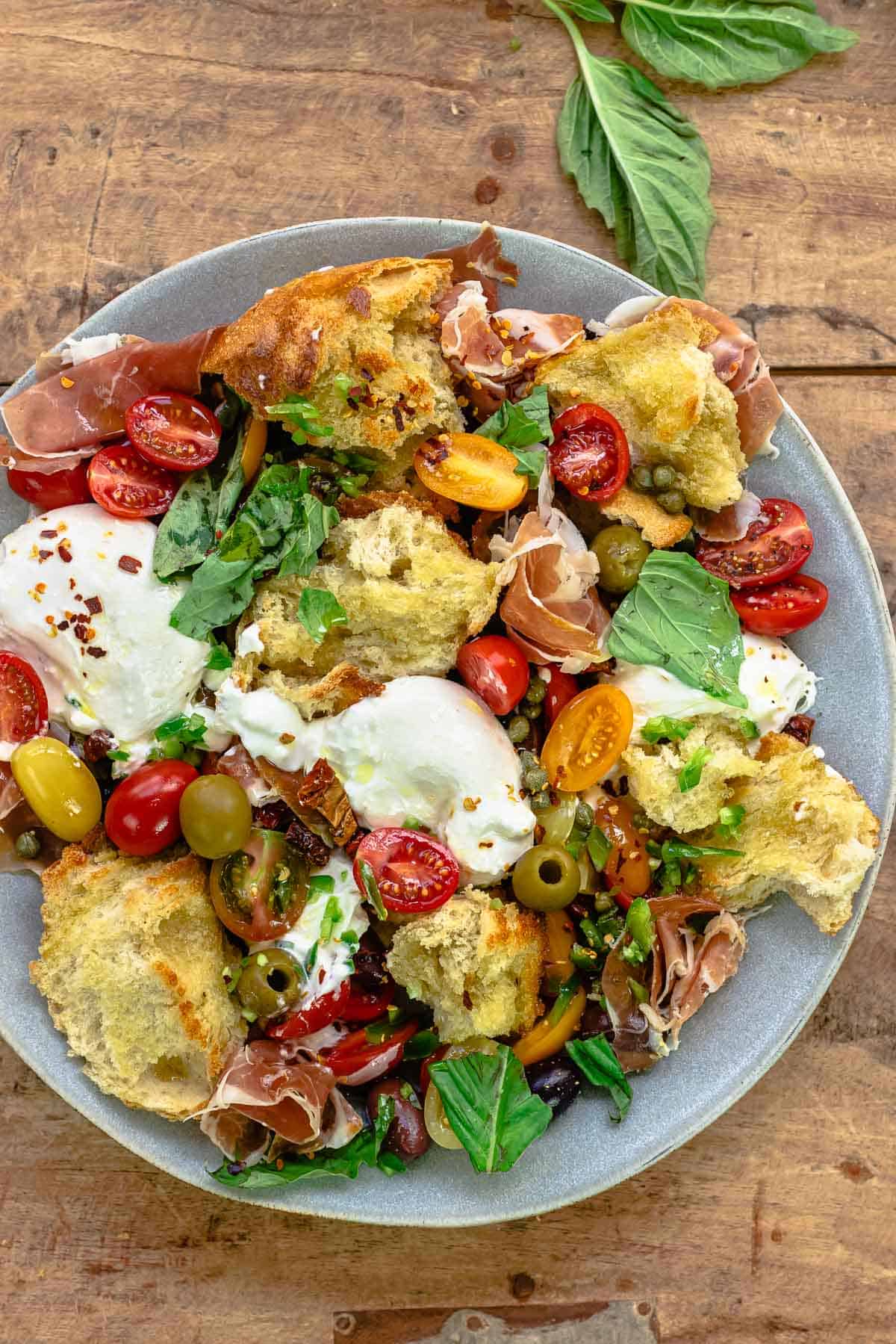 burrata salad on a gray plate with some fresh basil leaves on the side.