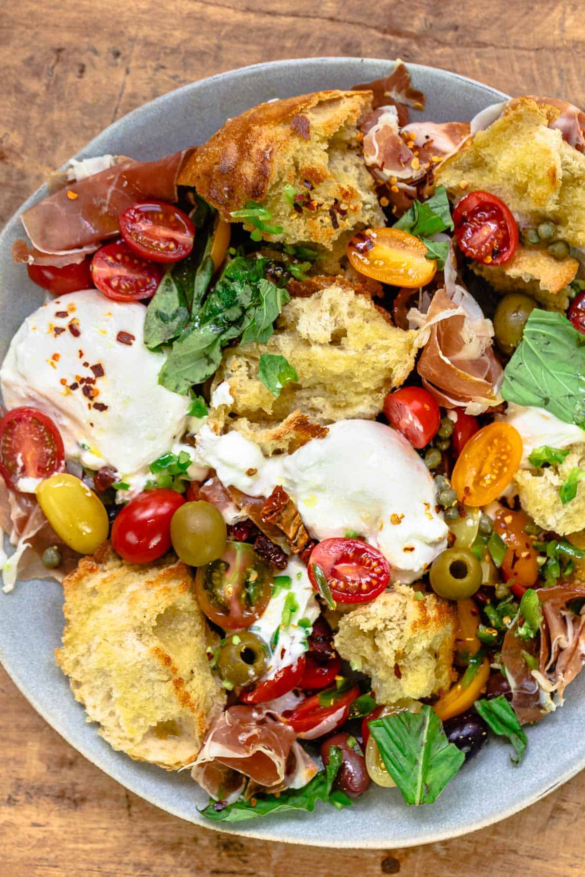 burrata with vegetables, prosciutto, and toasted ciabatta on a plate.