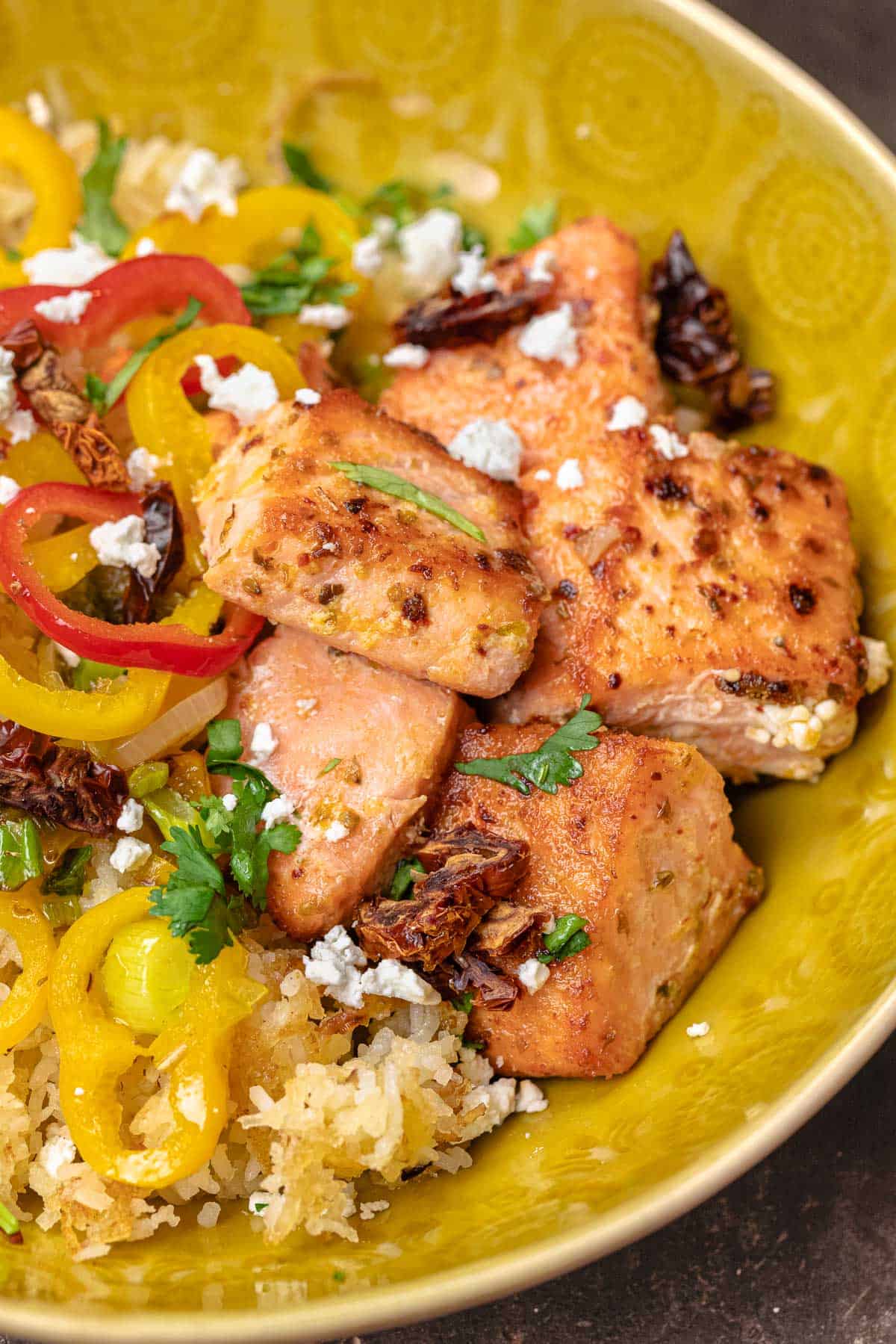 close up of salmon rice with feta cheese, parsley, and vegetables in a yellow bowl