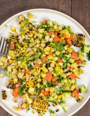 corn salad with cucumber, carrots, and fresh herbs on a white plate with a fork.