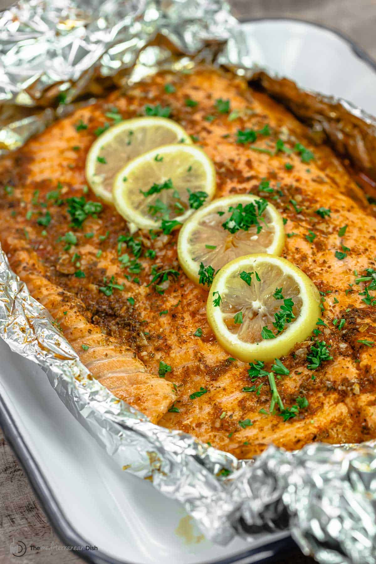 seasoned center cut fillet of salmon on a large piece of foil, topped with lemon slices and fresh herbs.