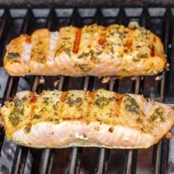 2 pieces of grilled salmon on the grill with the charred flesh side facing up.
