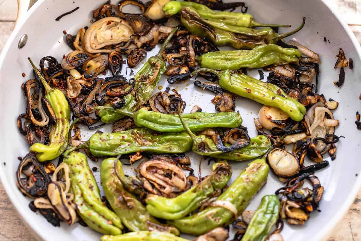 charred shallots and blistered shishito peppers in a pale skillet