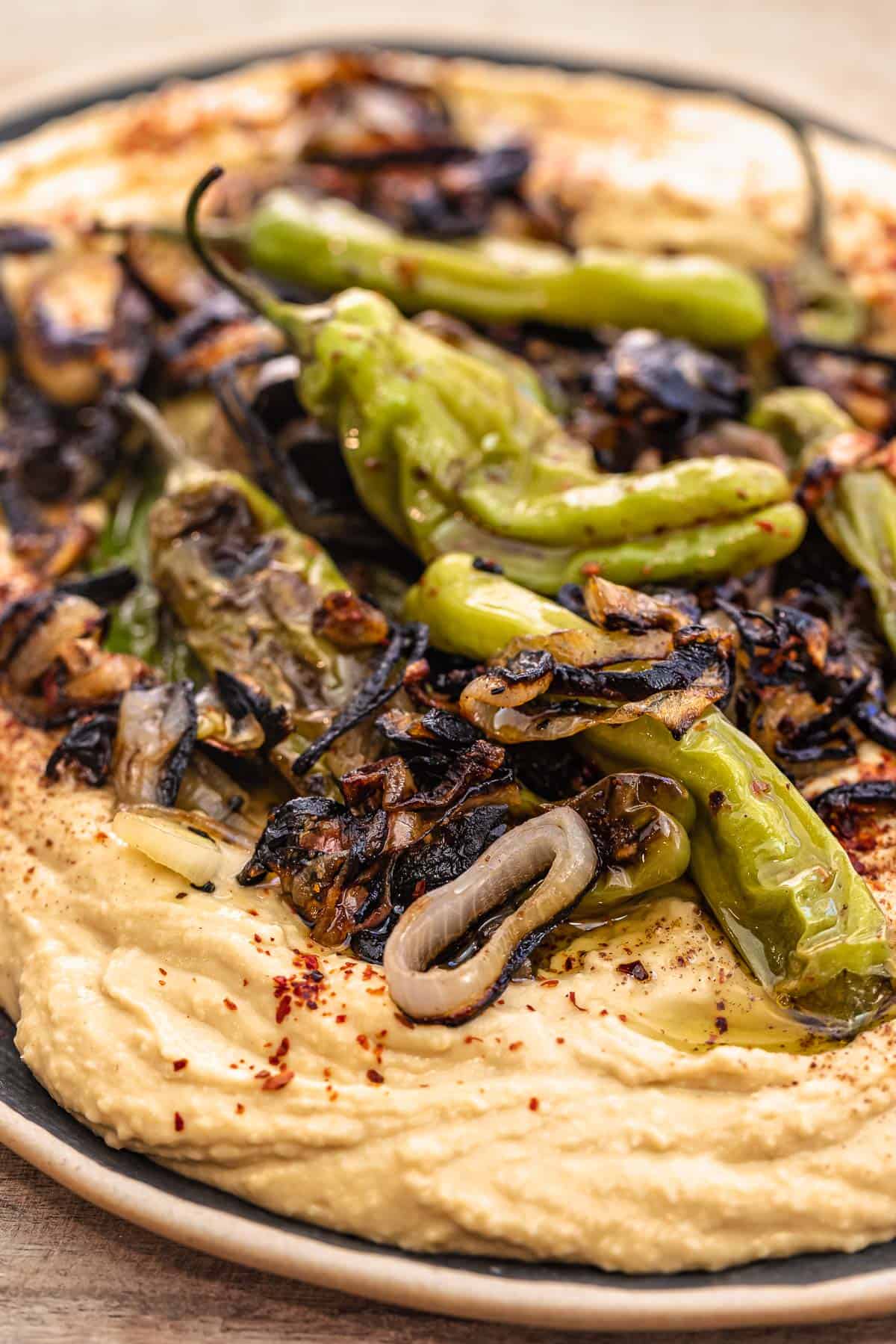 close up of hummus toppings: shallots and shishito peppers piled on top of creamy hummus