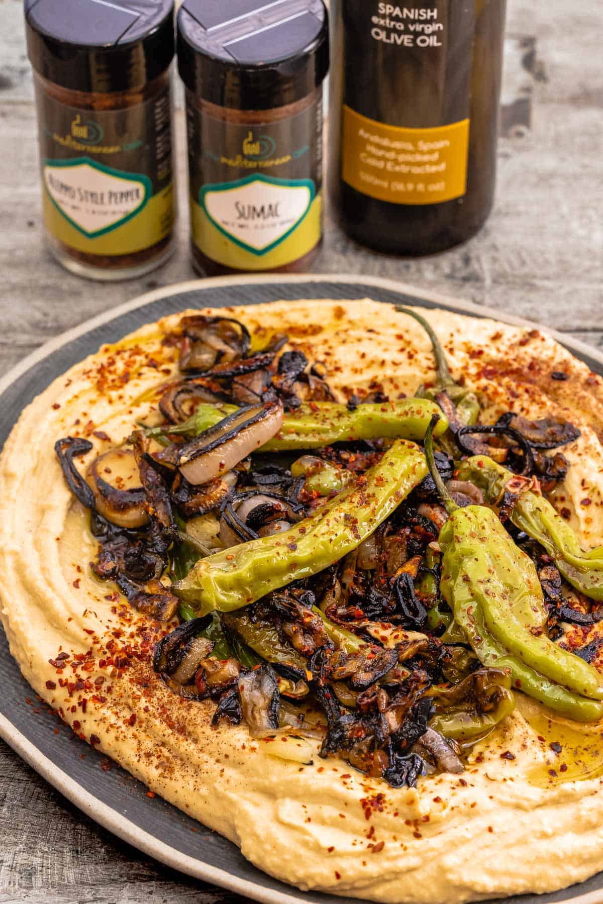 hummus with hummus toppings like shishito peppers and shallots. Aleppo-style pepper, sumac, and extra virgin olive oil in the background