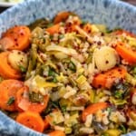 Braised leeks in a blue bowl with lemon wedges in the background.