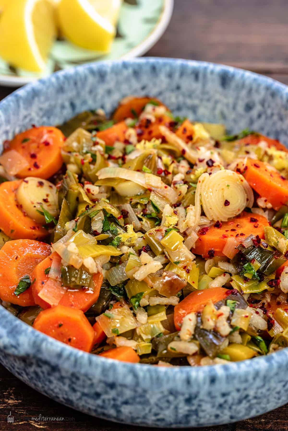 Braised leeks in a blue bowl with lemon wedges in the background.