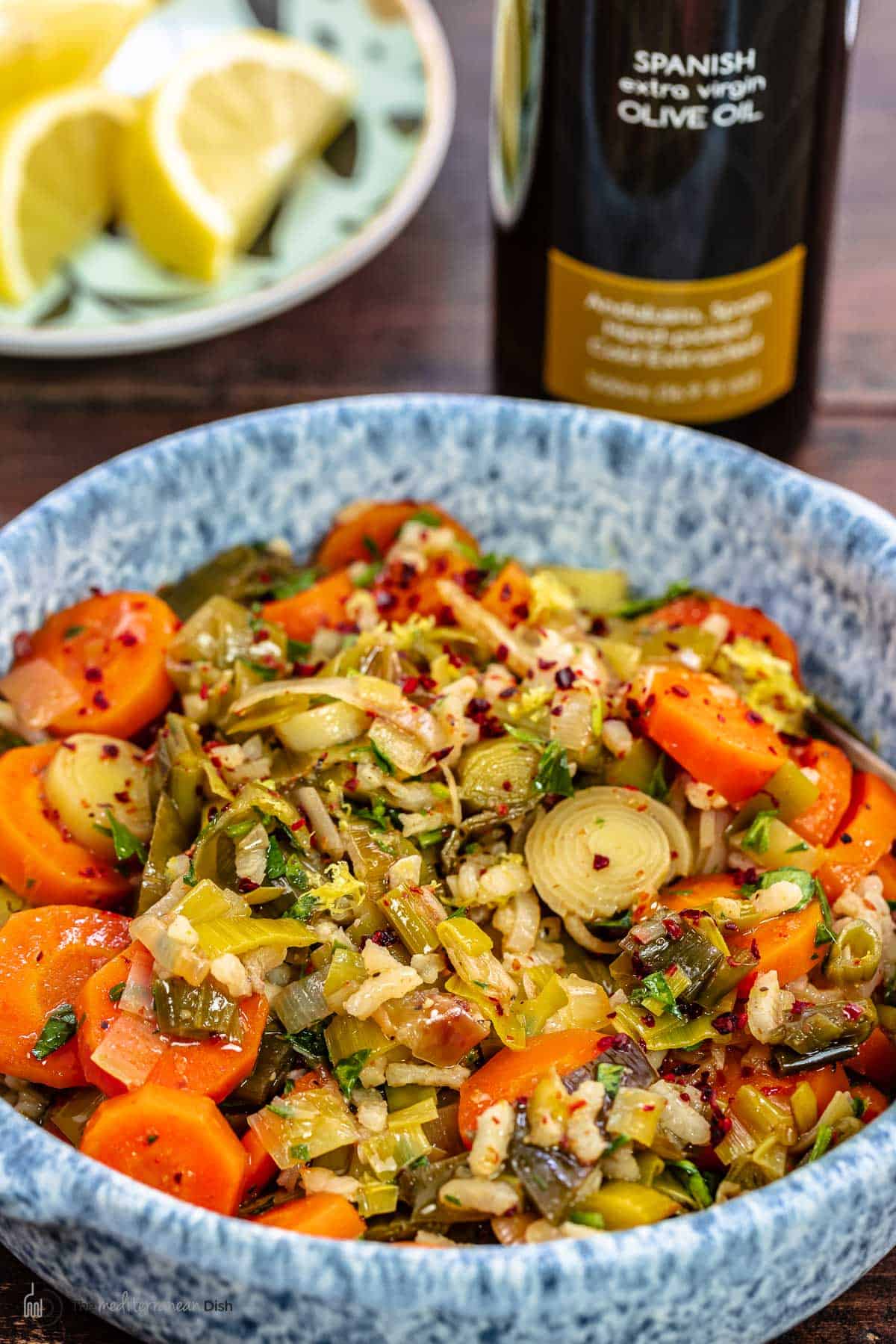 braised leeks and carrots with olive oil and lemon wedges in the background.