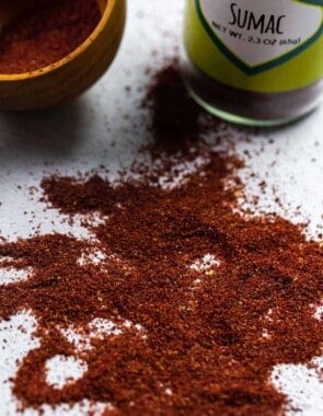 sumac spice sprinkled onto a flat surface with The Mediterranean Dish sumac and a container in the background.