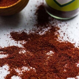 sumac spice sprinkled onto a flat surface with The Mediterranean Dish sumac and a container in the background.