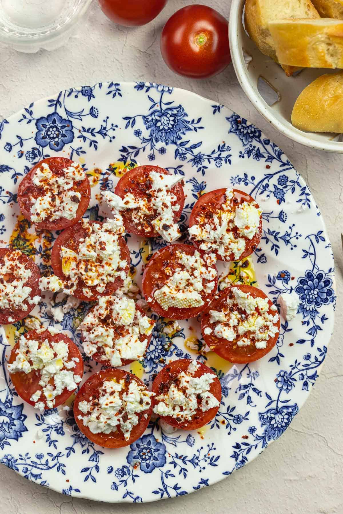 Tomato halves with feta crumbled feta on a blue and white plate with a side of bread slices