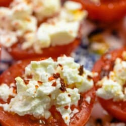 close up photo of sliced fresh tomato with crumbled feta and red pepper flakes