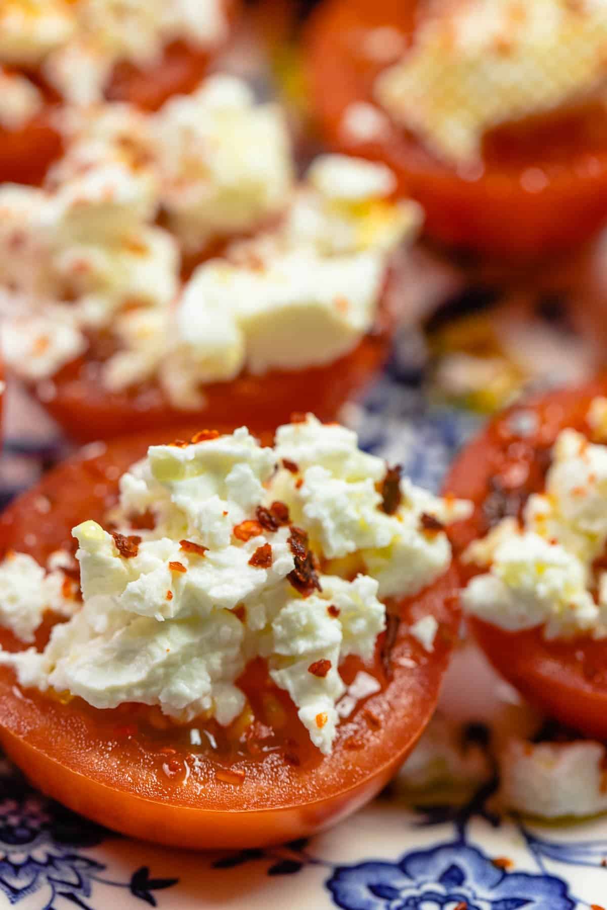 close up photo of sliced fresh tomato with crumbled feta and red pepper flakes