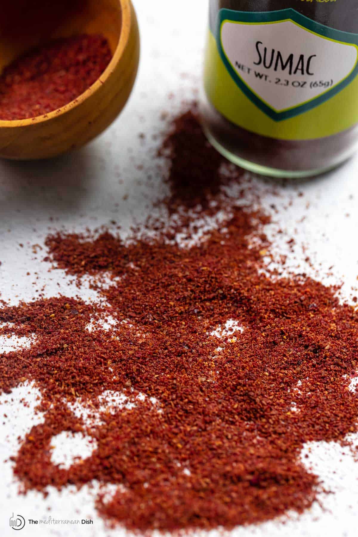sumac spice sprinkled onto a flat surface with The Mediterranean Dish sumac and a container in the background.