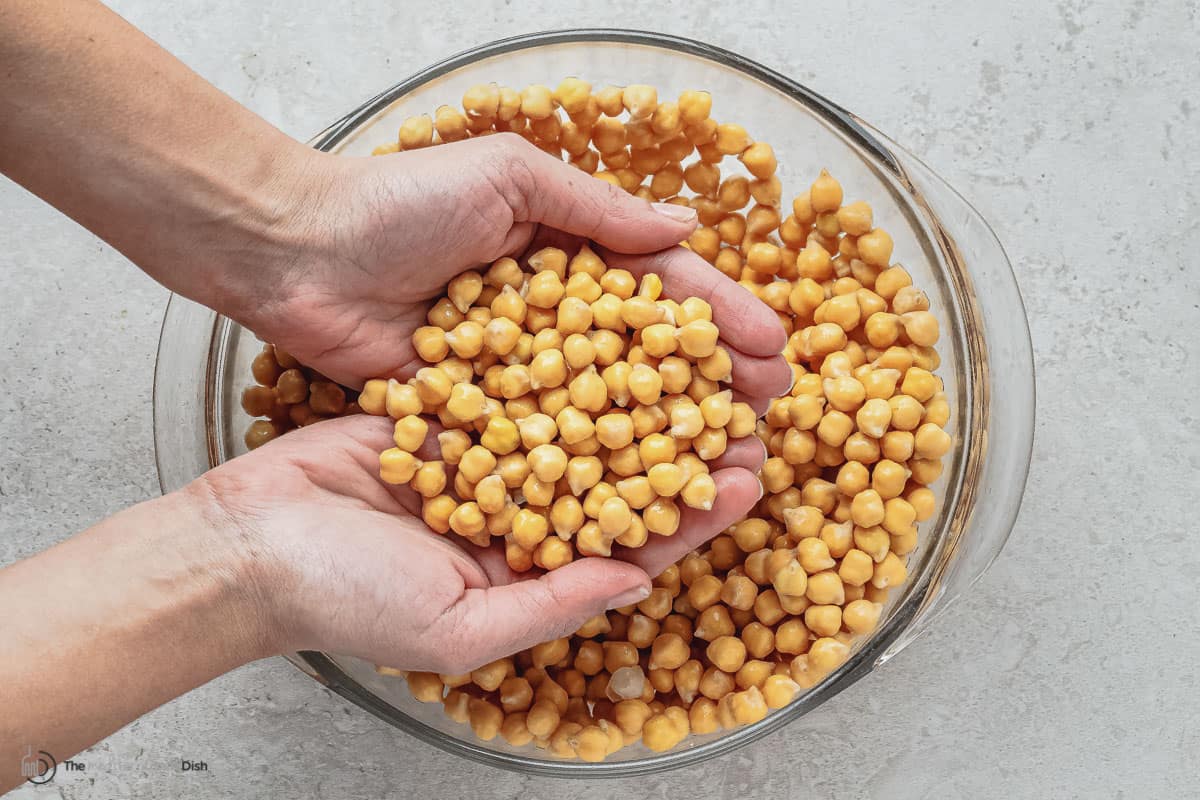 soaked chickpeas in a bowl with a woman holding some in her hands.