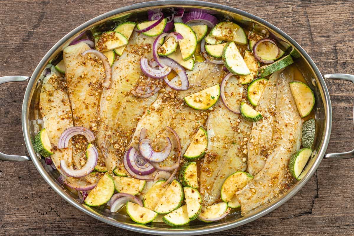 flounder fillets with sliced vegetables and sauce in a baking pan.