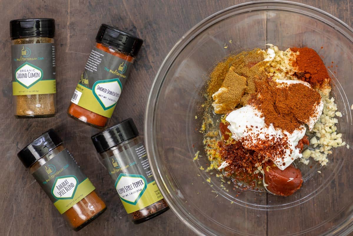 ingredients for doner kebab marinade including cumin, smoked paprika, Baharat spice blend, Aleppo-style pepper, whole milk yogurt, garlic, lemon juice, lemon zest, and tomato paste.