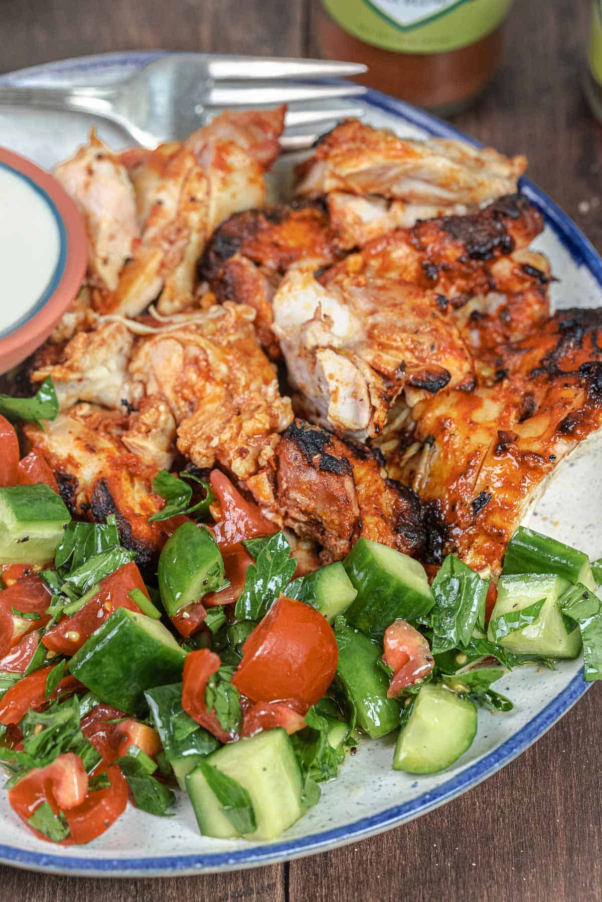 doner kebab on a plate with tomato and cucumber salad with a small bowl of sauce on the side.