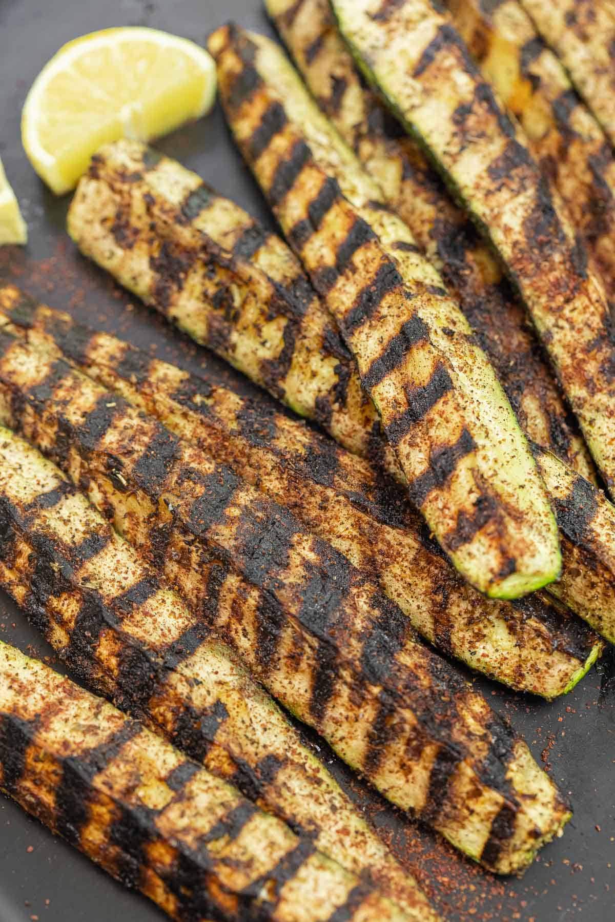 close up of grilled zucchini with some sumac sprinkled on top, with lemon slices on the side.
