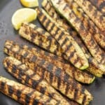 grilled zucchini with char marks on a plate with lemon slices.