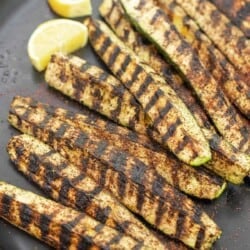 grilled zucchini with char marks on a plate with lemon slices.