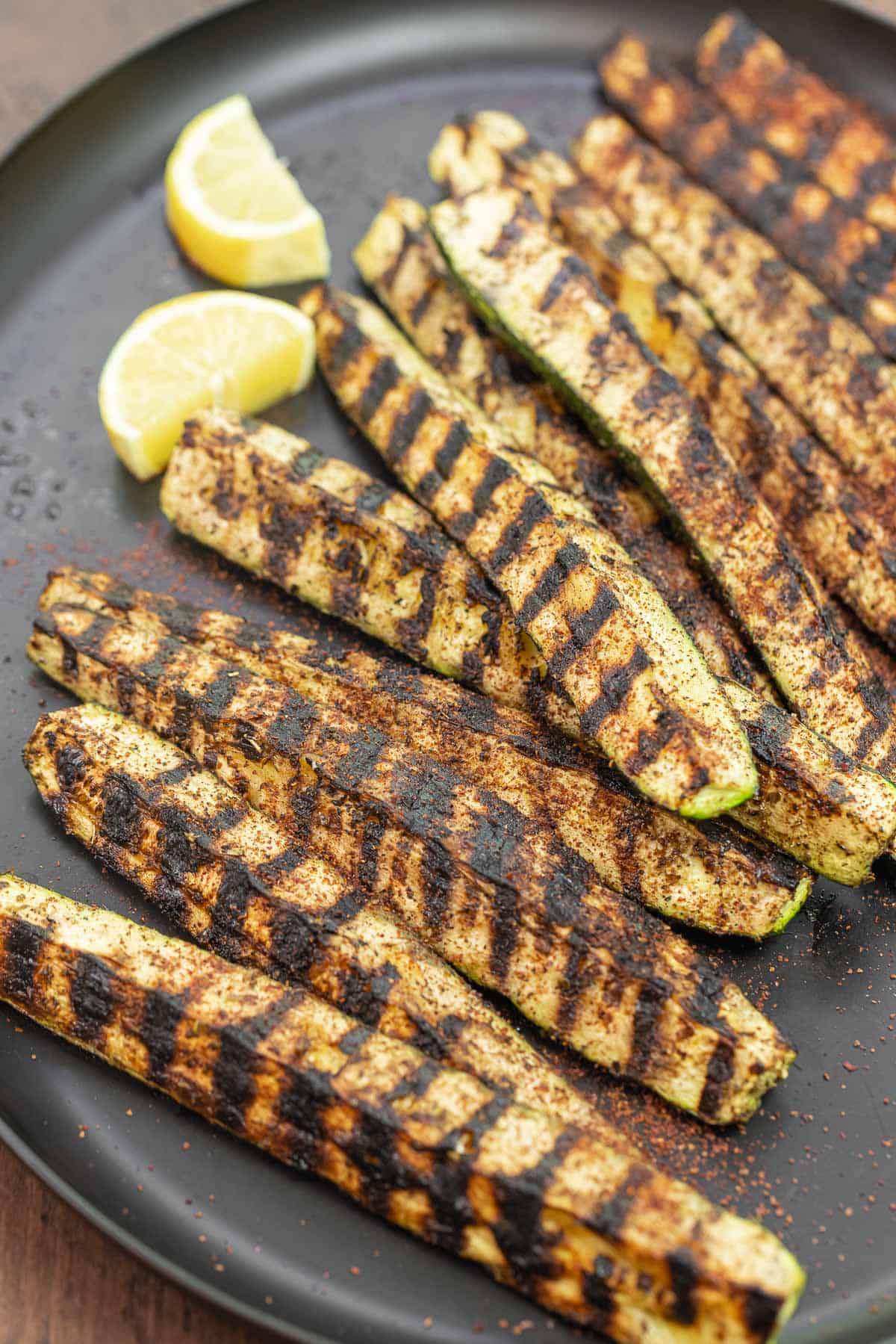 grilled zucchini with char marks on a plate with lemon slices.