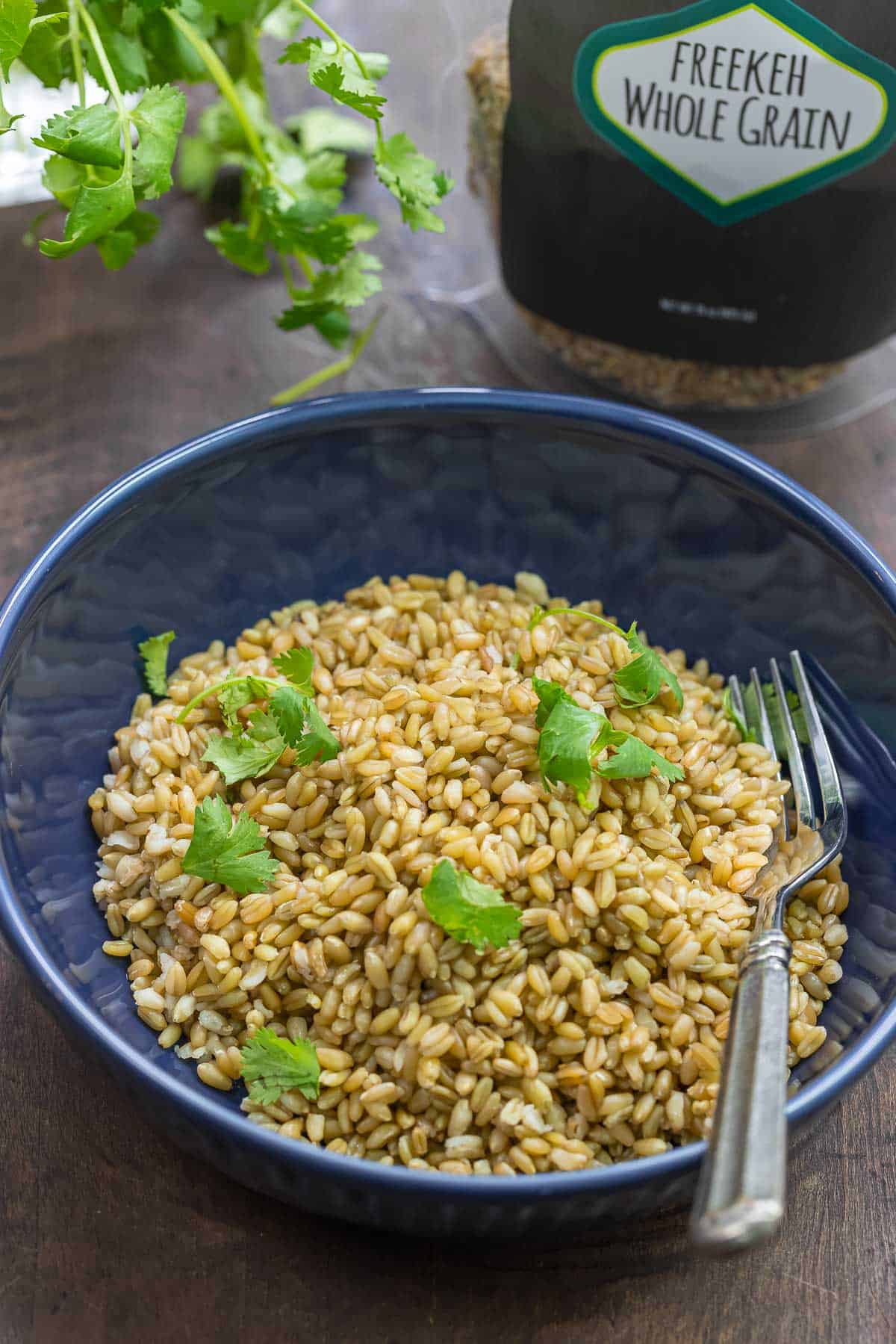 cooked freekeh in a bowl sprinkled with fresh parsley. The Mediterranean Dish wholegrain freekeh in the background.