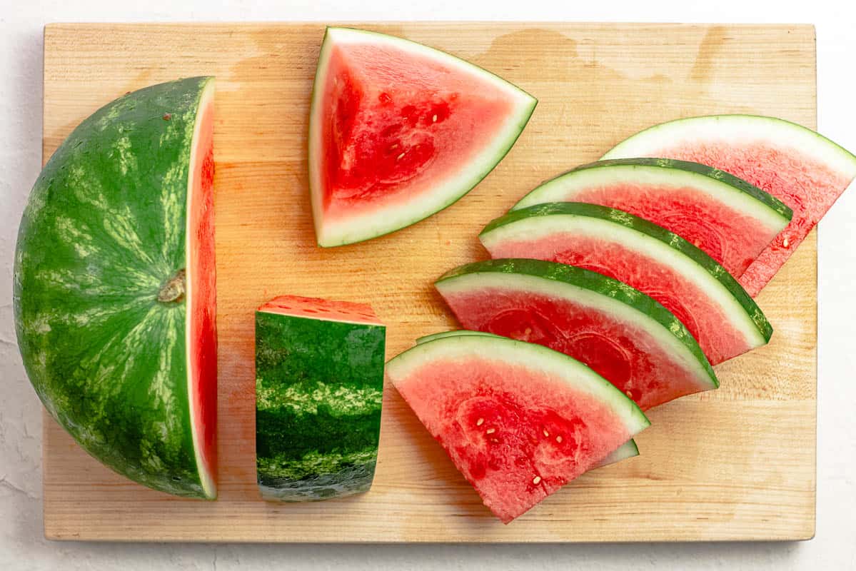step image for how to cut a watermelon into wedges: a watermelon cut into several wedges on a cutting board.