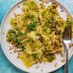 pesto ravioli recipe with peas, toasted pine nuts, and Aleppo pepper flakes on a plate with a fork.