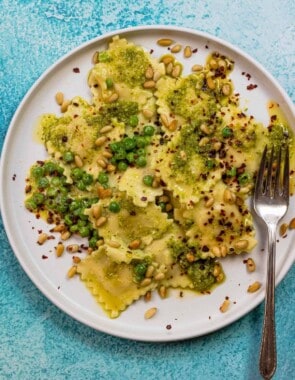 pesto ravioli recipe with peas, toasted pine nuts, and Aleppo pepper flakes on a plate with a fork.