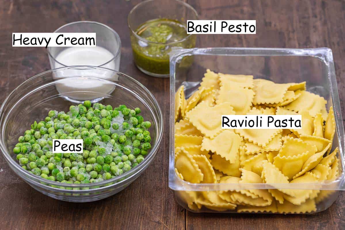 labeled ingredients for pesto ravioli recipe including basil pesto, heavy cream, frozen peas, and four-cheese ravioli.