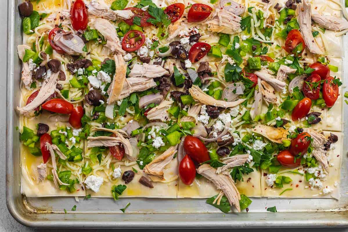 close up of phyllo pizza crust with pizza toppings like chicken, shallots, grape tomatoes, olives, and bell peppers.