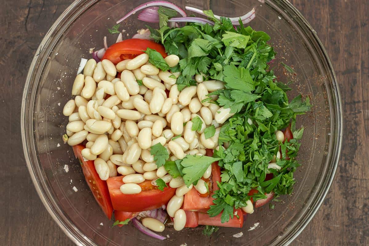 Turkish white bean salad ingredients combined in a bowl including white beans, fresh parsley, tomatoes, red onion, and garlic.