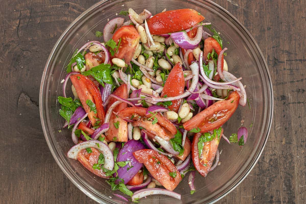 Piyaz tossed with a simple dressing in a glass bowl.