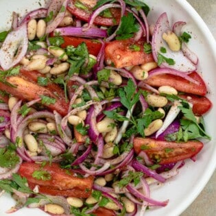 Turkish white bean salad with onions and tomatoes on a deep white plate with sumac alongside.